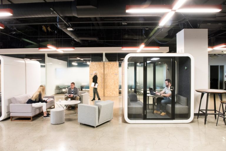 A man inside Framery Q, people chatting outside the pod in the office.