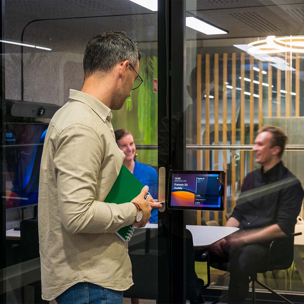 Person entering a meeting in a Framery 2Q meeting room with a Logitech Tap Scheduler on the door.