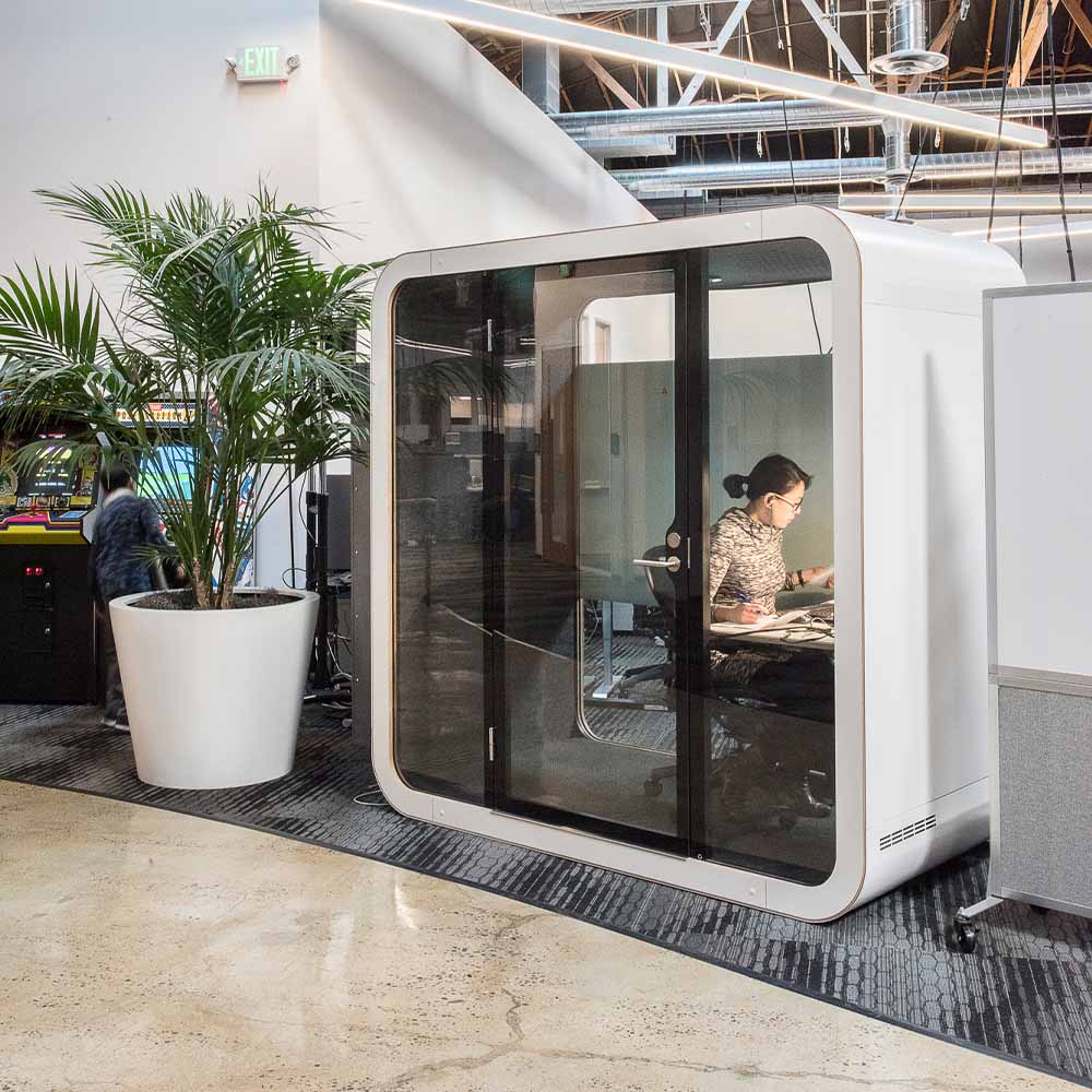 A person working in a Framery Q Flow meeting pod in a hallway of an office building.