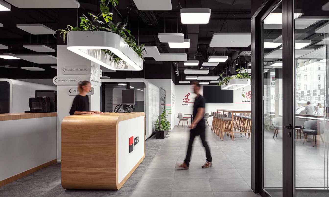 Person walking to a counter in KB Bank office with a Framery 2Q meeting room in the background.