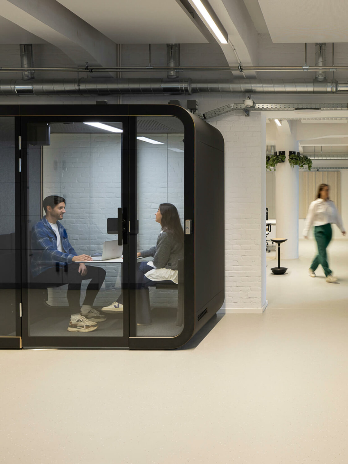 A Framery pod with black exterior in a white office setting as background.