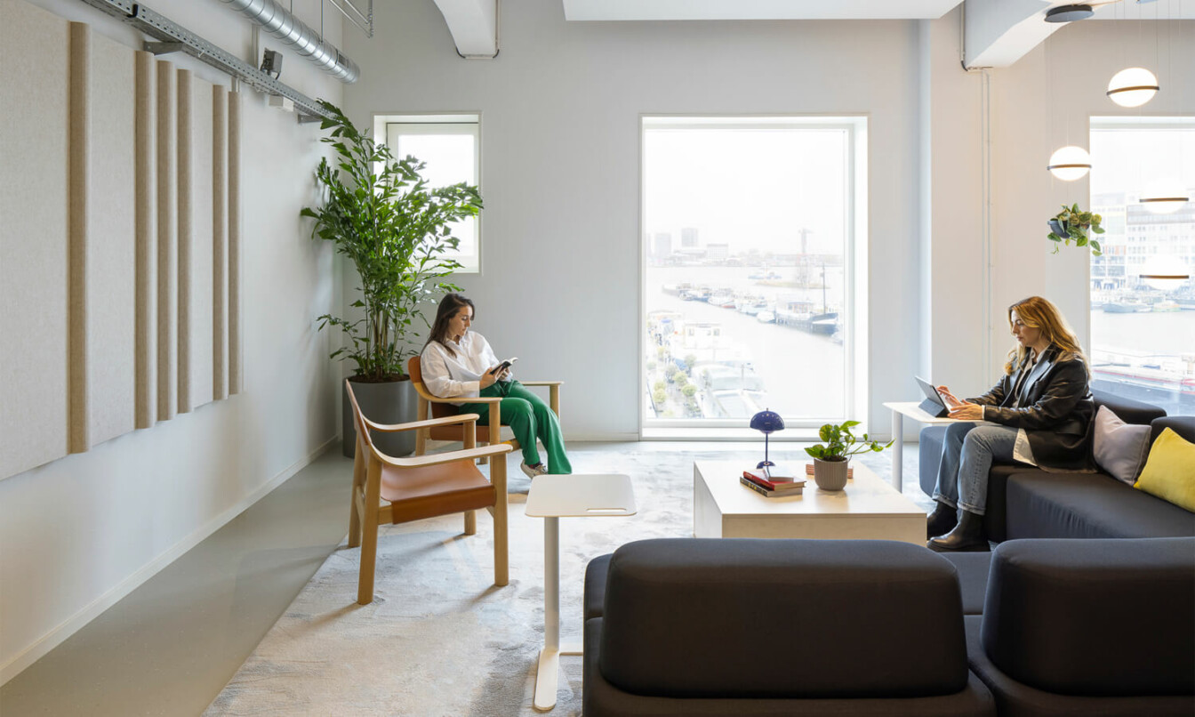 A light office lobby with sofa and armchair and two women sitting and working.