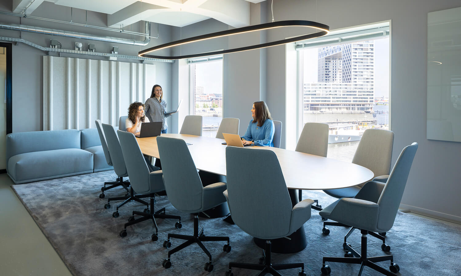 Three happy women around a meeting table in a meeting room with light blue interior design.