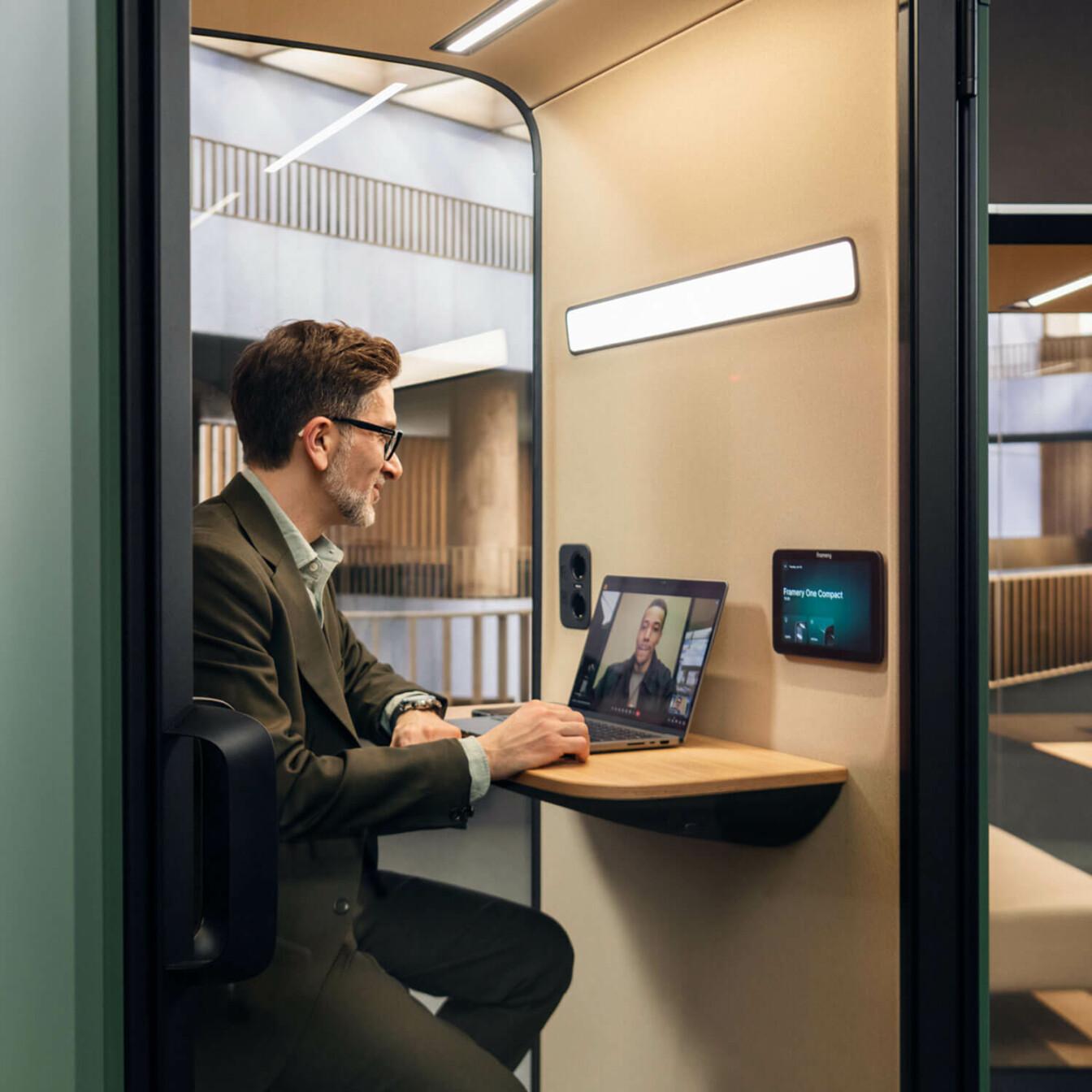 A person in a video meeting within a Framery One Compact, office phone booth.