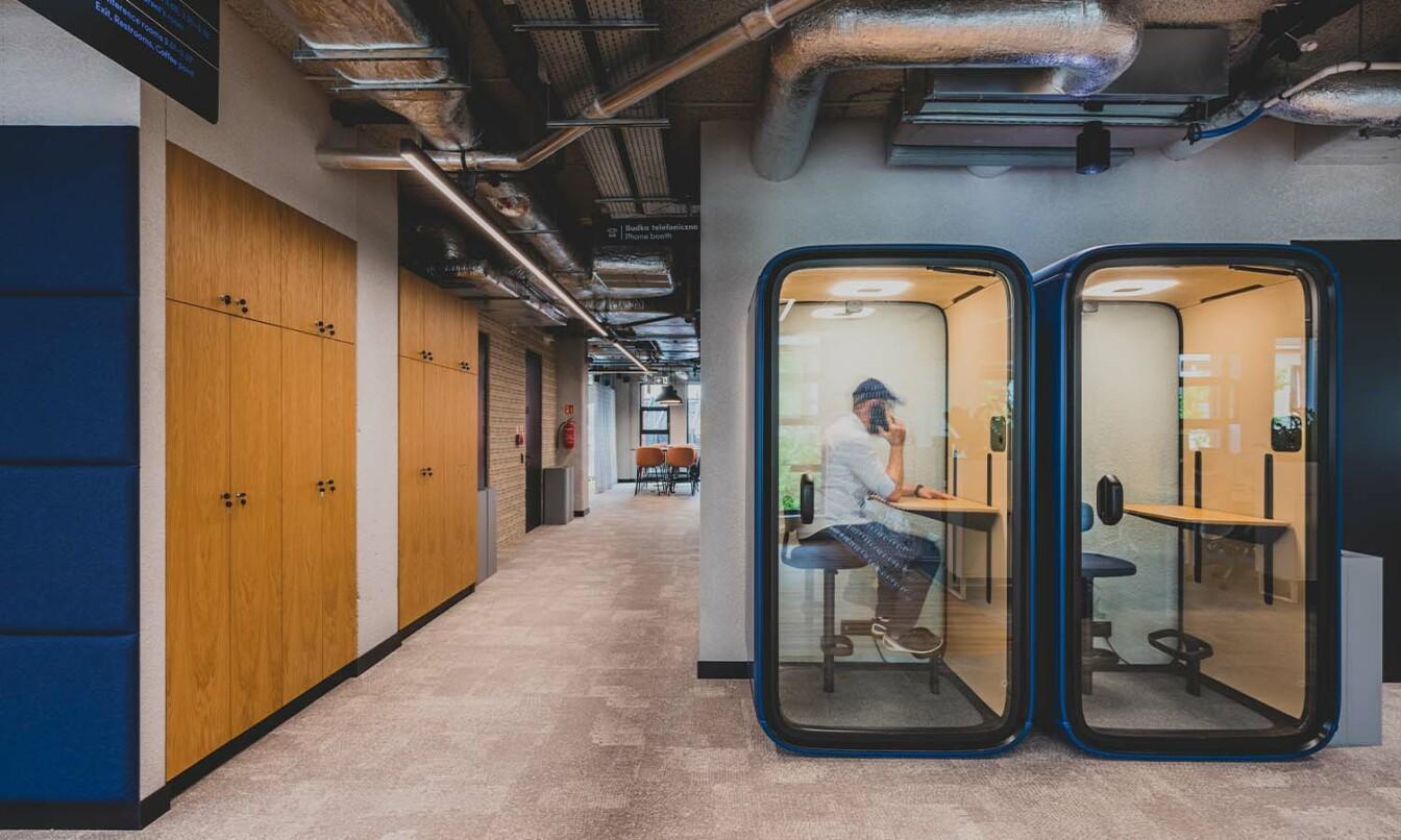 Two blue Framery One pods at an office with a person takin a phone call inside one pod.