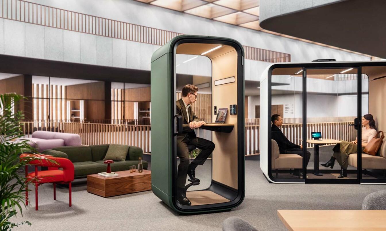 People in modern office furniture, Framery smart pods having in-person and virtual meetings.