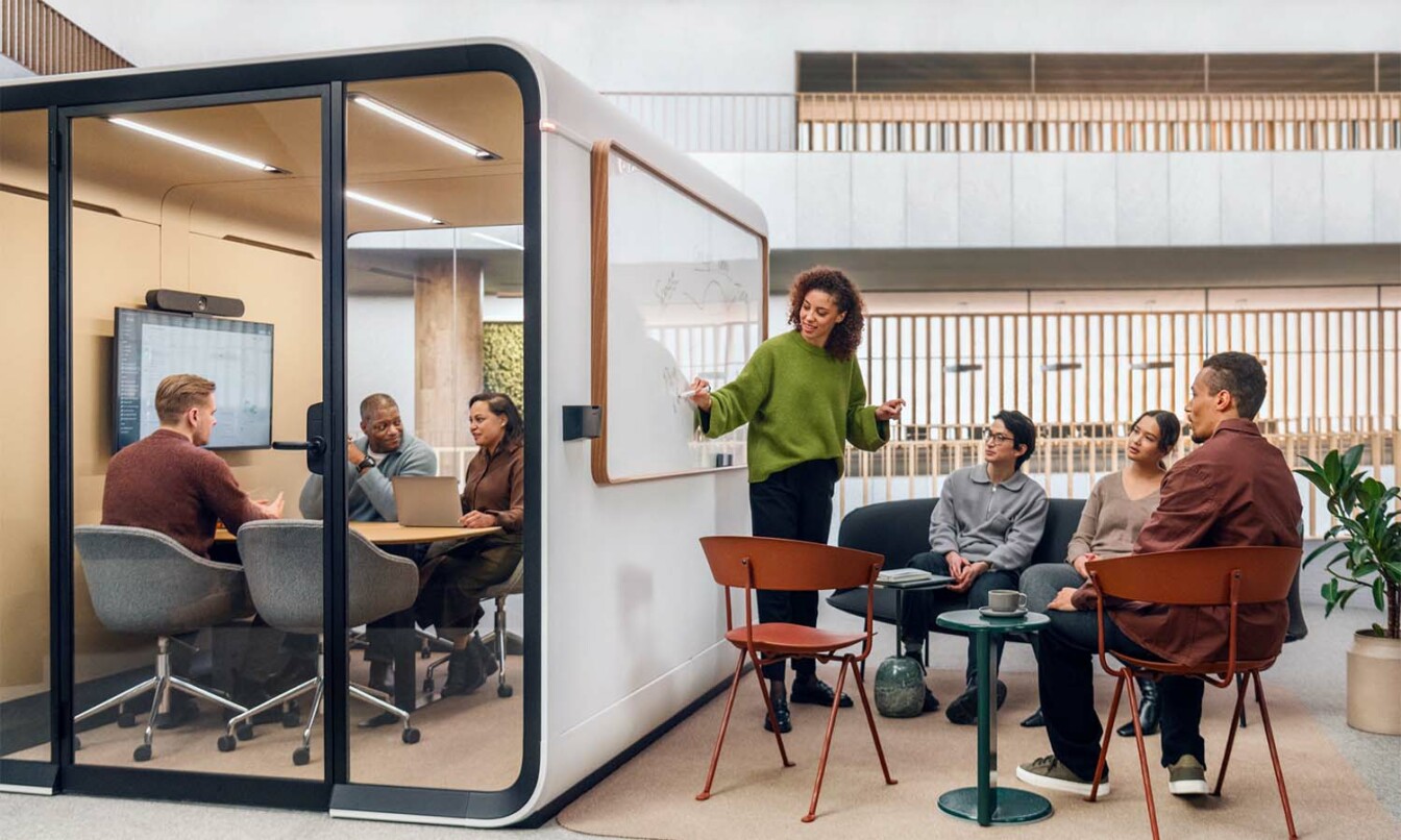 People having a meeting within and next to a Framery Six meeting room.