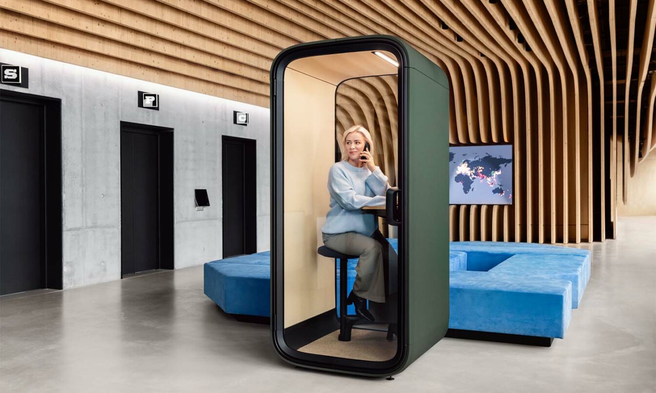 A person in a phone call inside a Framery One Compact call pod in a hallway.