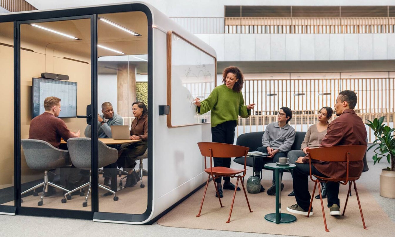 People working inside the Framery Six meeting room and next to it in a gather zone.