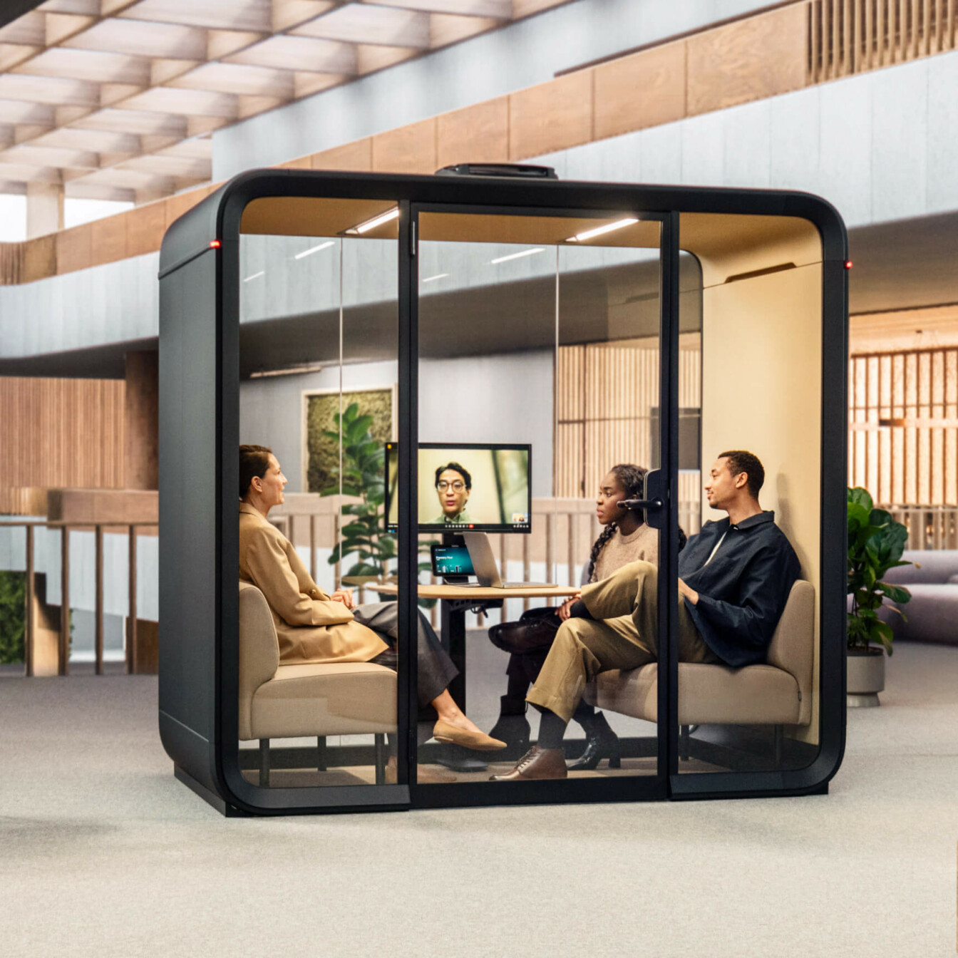 Three people sitting inside a meeting pod in an office.