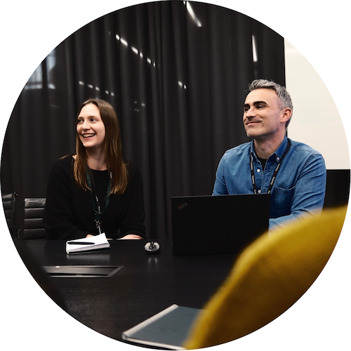 Smiling woman and man sitting behind an office table with laptops on the table.