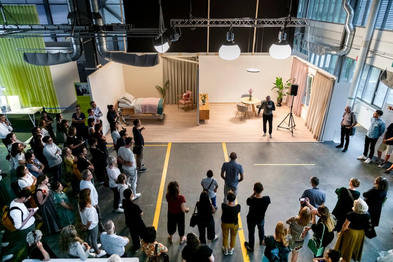 A crowd of people in a hall looking at two model healthcare rooms.