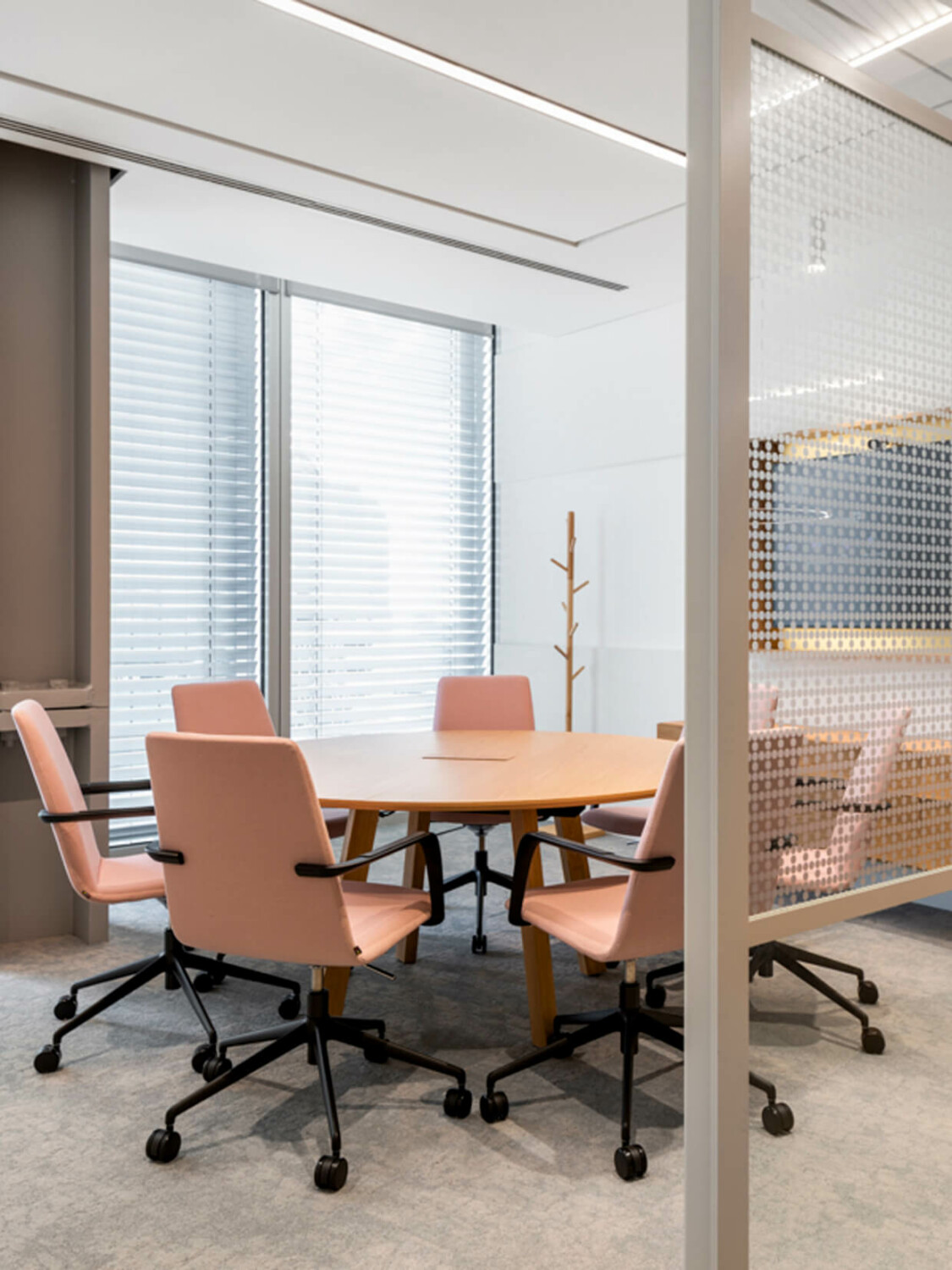 A light colored meeting room in an office with a round table and pink meeting chairs.