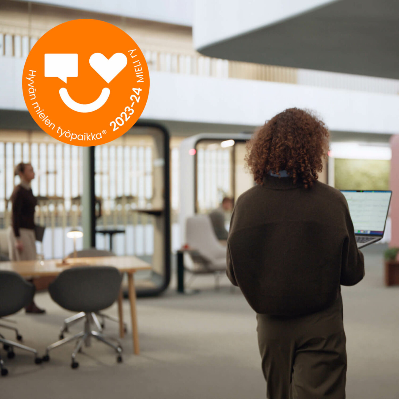 Woman with back facing the camera walking in an office with pods in the background.