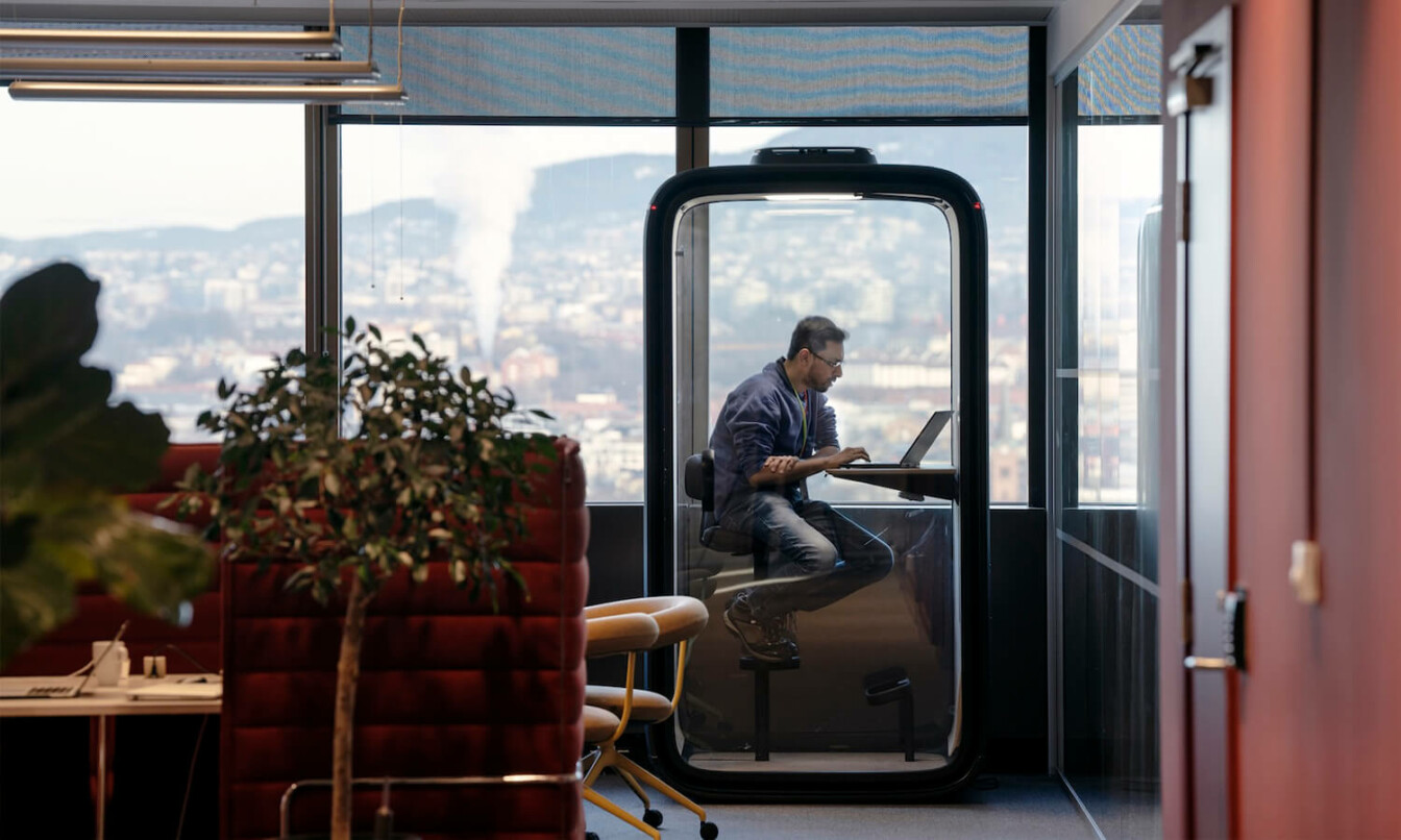 Man sitting in a Framery pod in a dark color office.