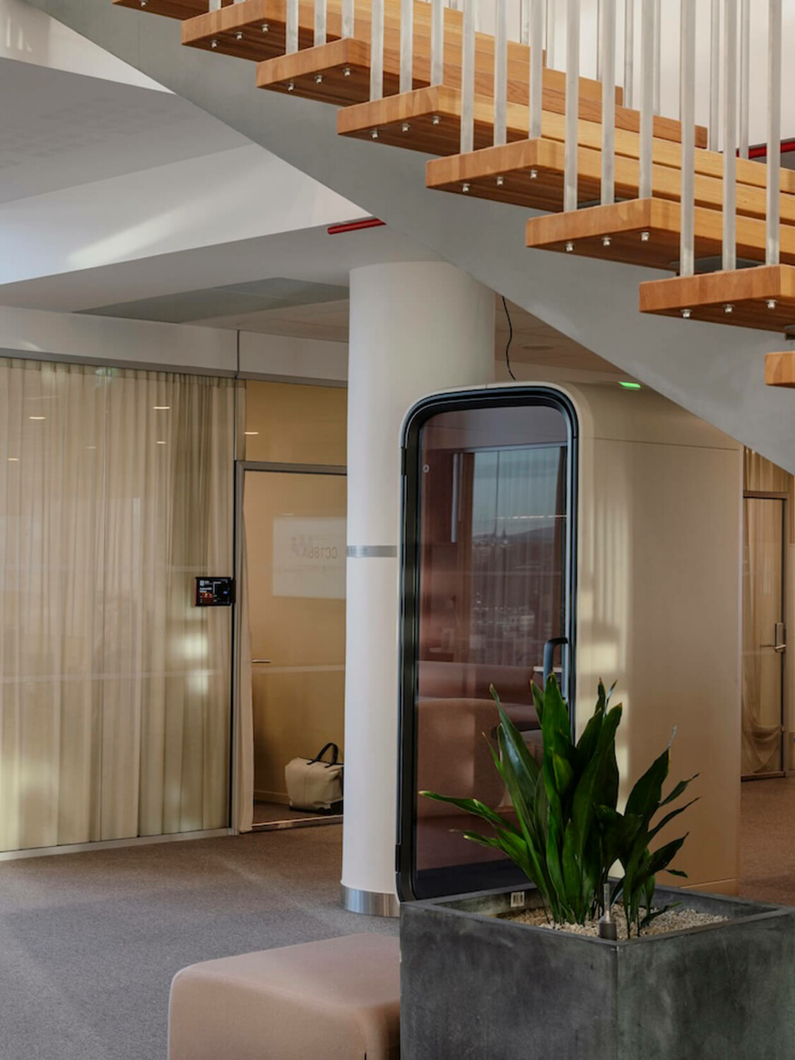 A beige Framery pod under an office staircase.
