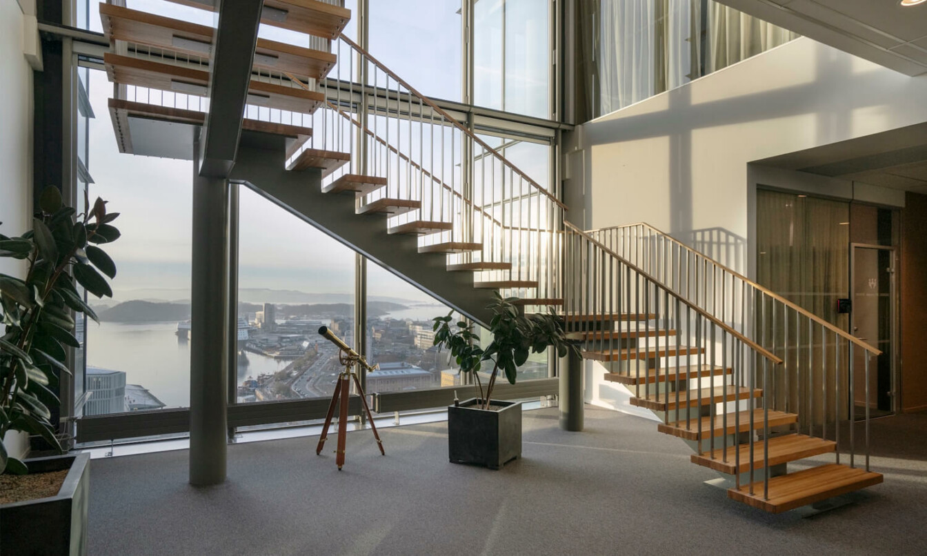 A modern wooden staircase in a an office hallway with big window behind.