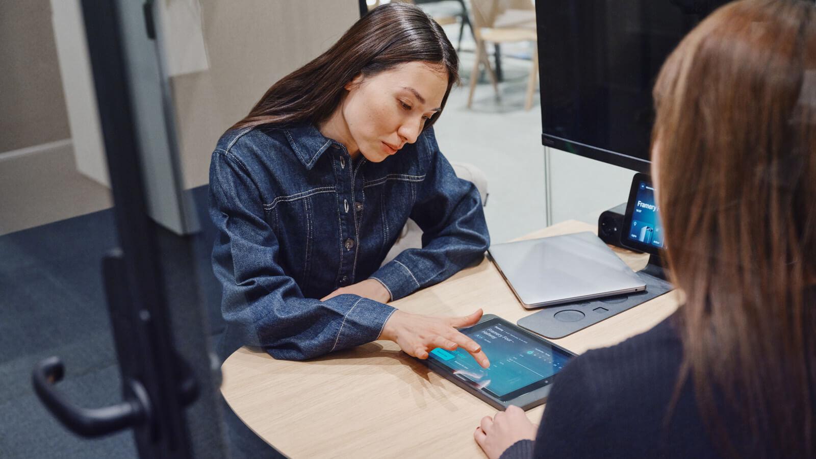 A woman working on a tablet on top of a table.