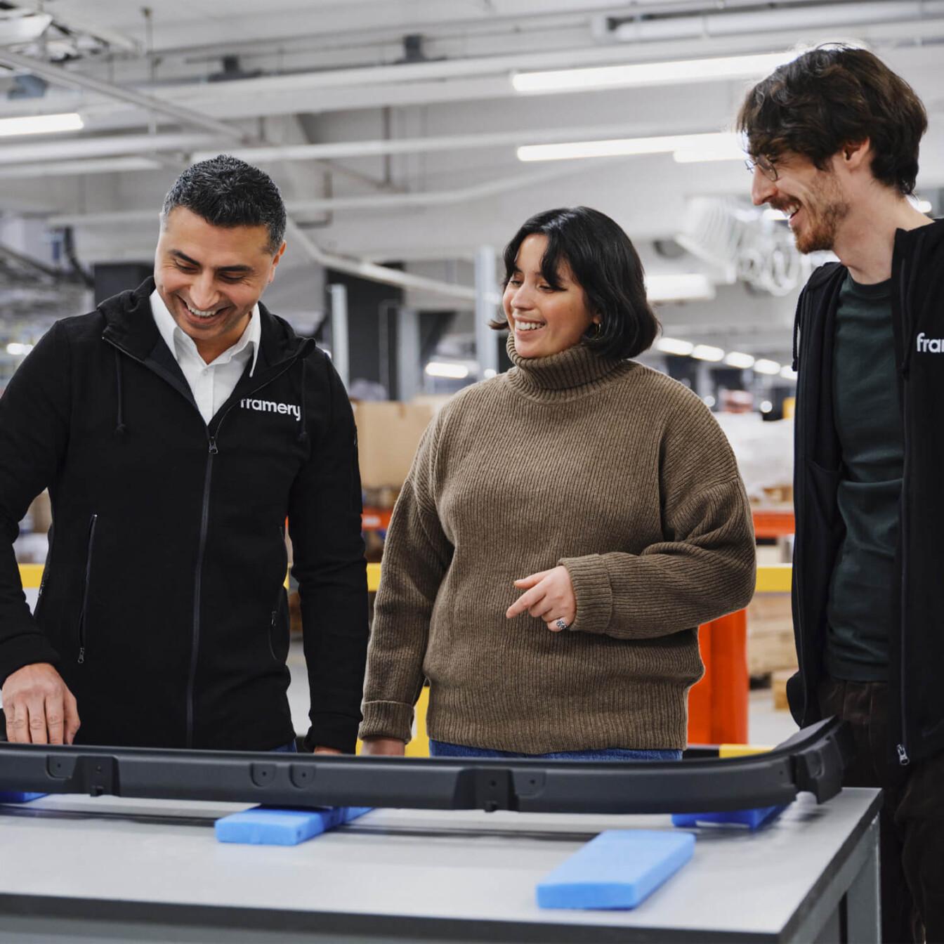 Three smiling people standing in front of a factory table.