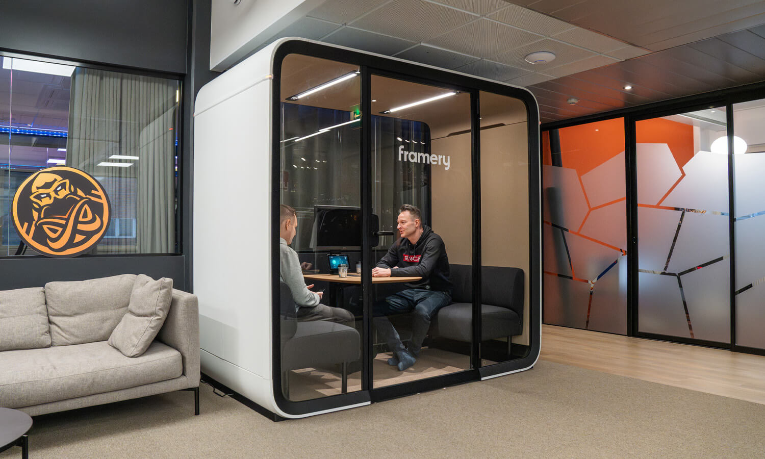 Two men sitting inside a white Framery pod inside an office.