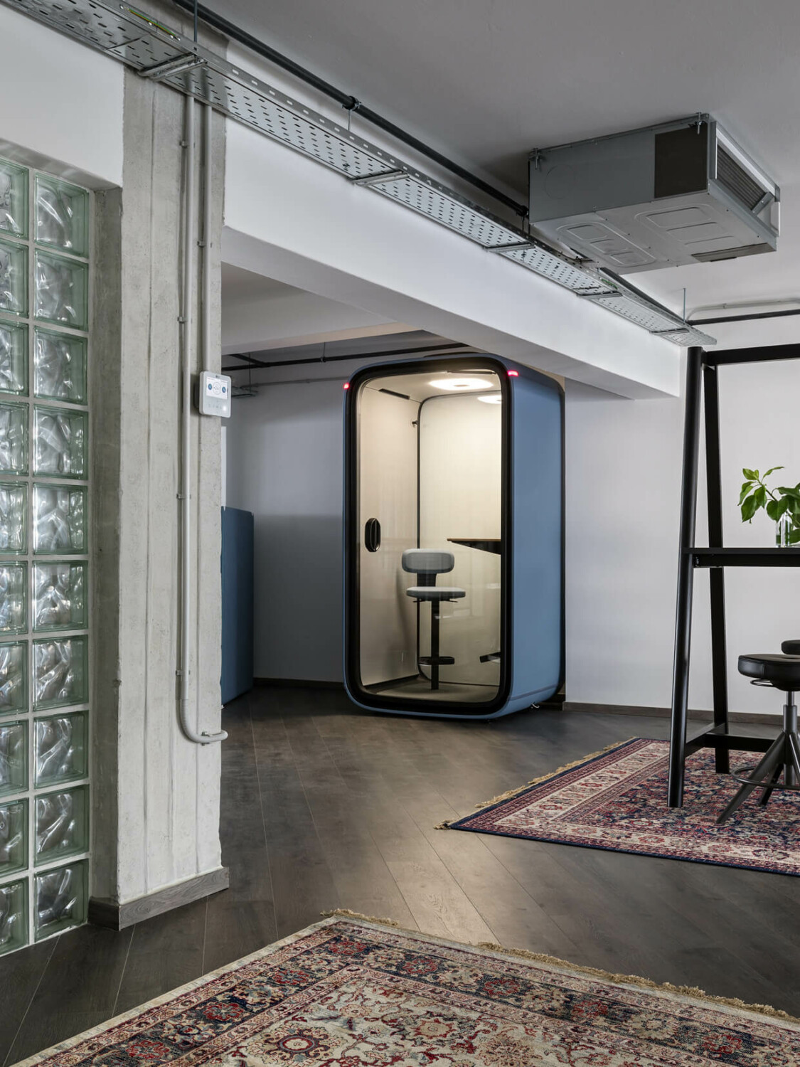 A light blue Framery pod in an office hallway with colorful carpets