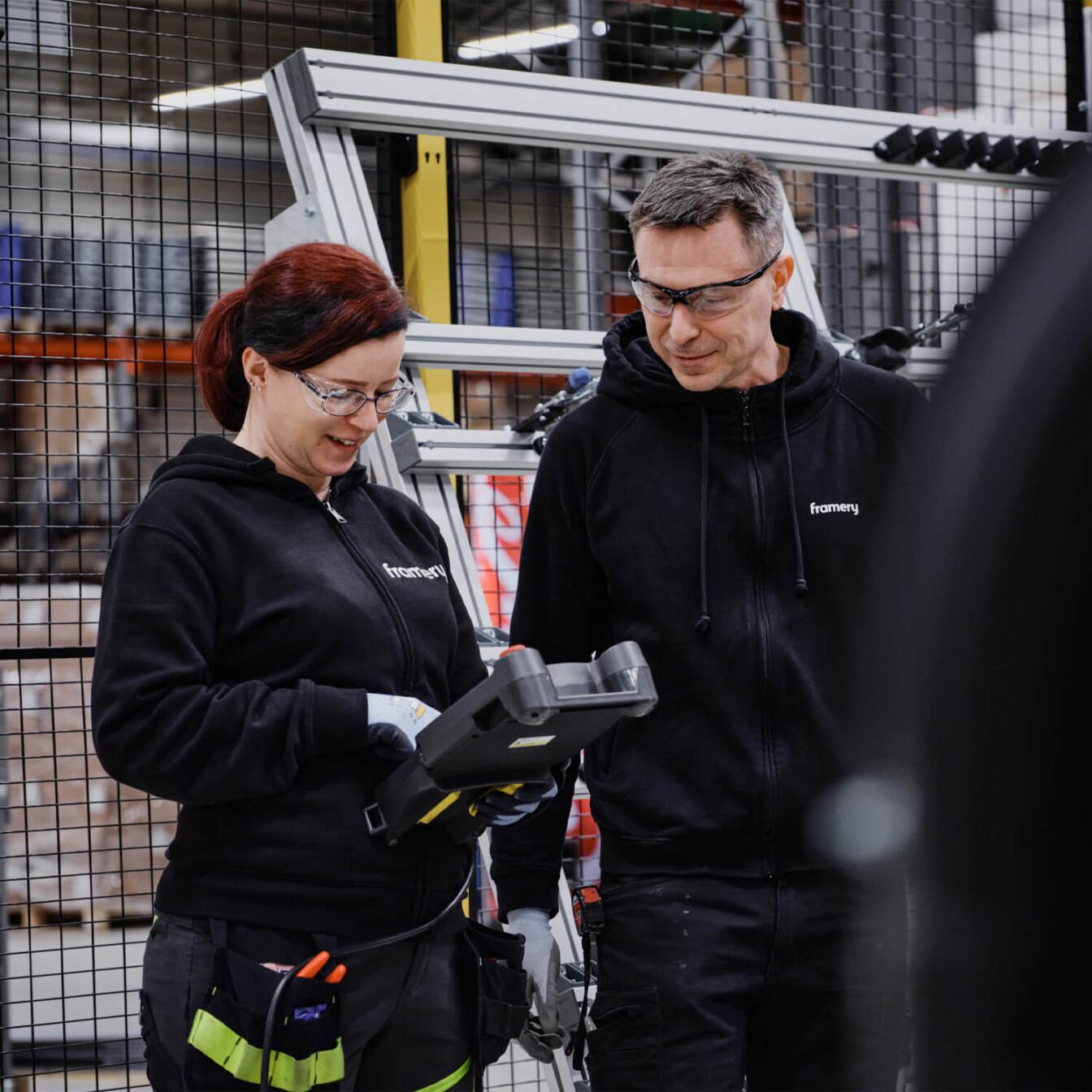 A woman and a man in black work wear in a factory setup.