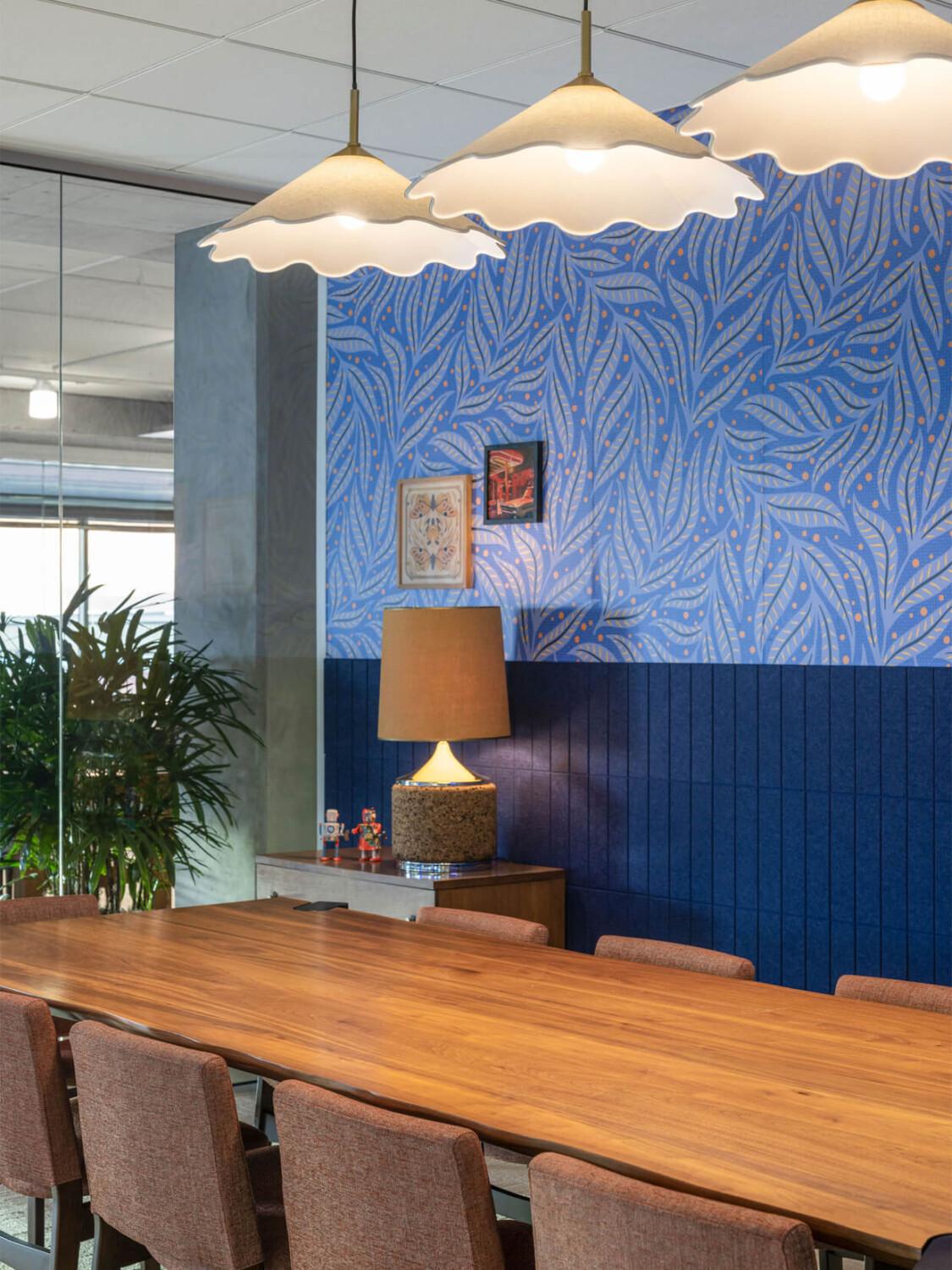 A long meeting room table with chairs and flower pendants and blue wallpaper.