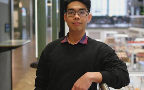 A man leaning one arm onto a railing inside an office and looking into the camera