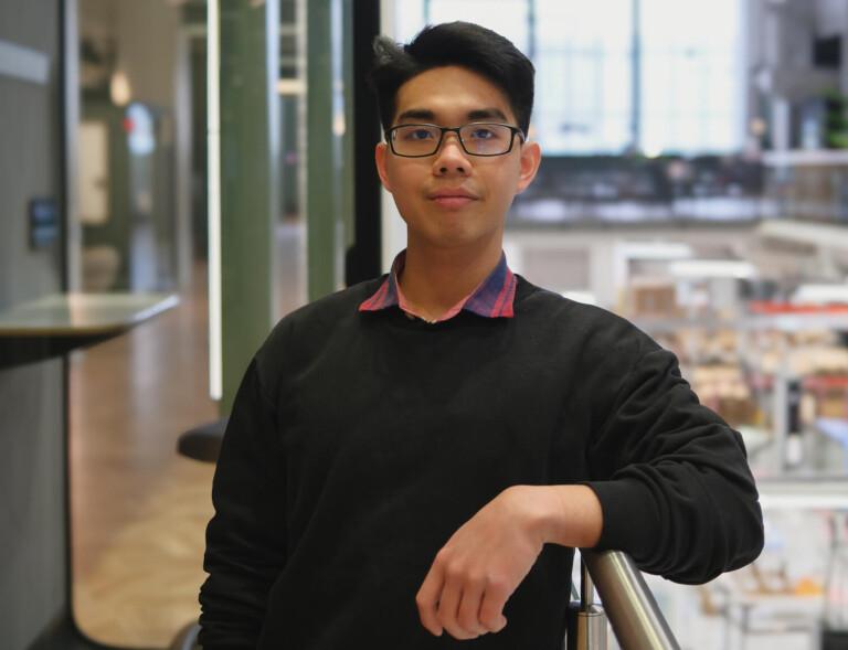 A man leaning one arm onto a railing inside an office and looking into the camera