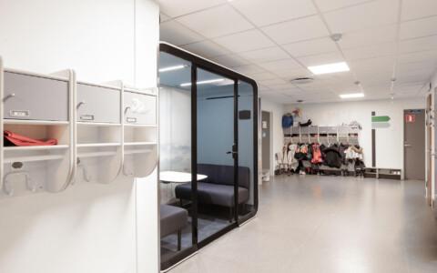 A light colored empty school hallway with a whit a study pod.