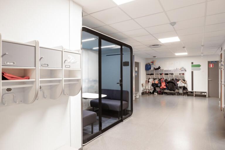 A light colored empty school hallway with a whit a study pod.