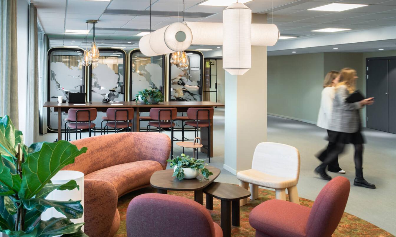 A red-toned office lounge area at front with Framery One office pods as a row in the back.