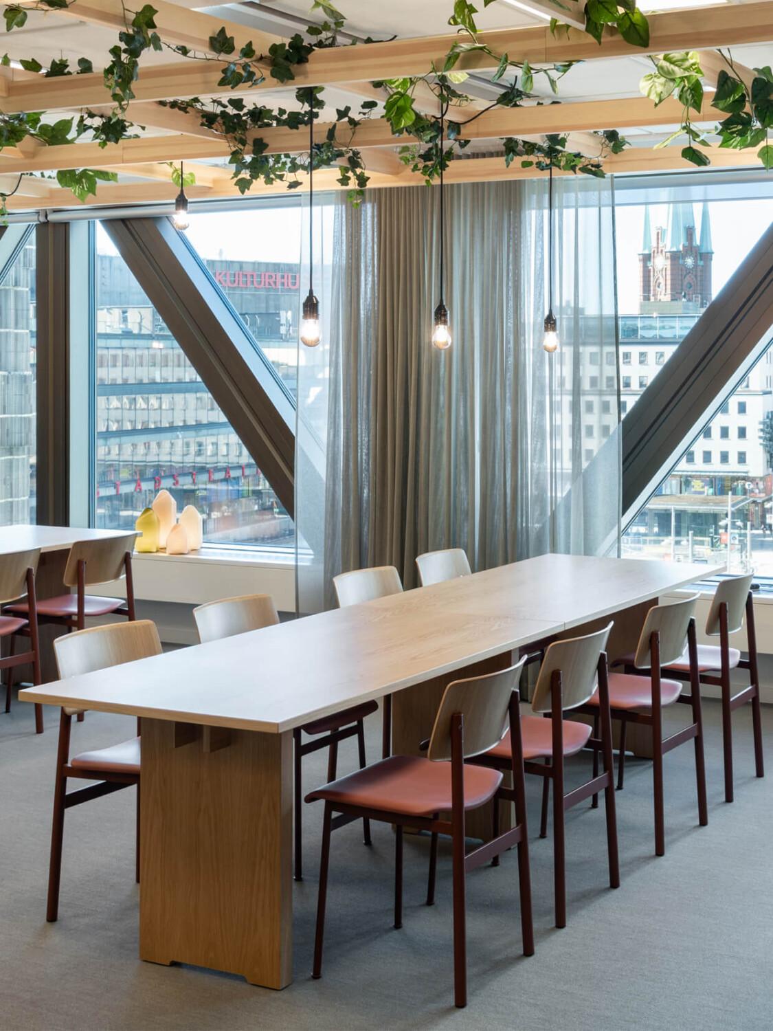 A long office cafeteria table with red chairs and a nice view outside.