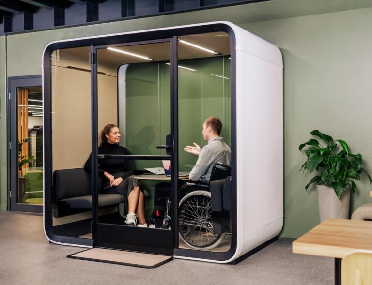 Two people, the other in a wheelchair, having a conversation in a wheelchair accessible meeting pod.