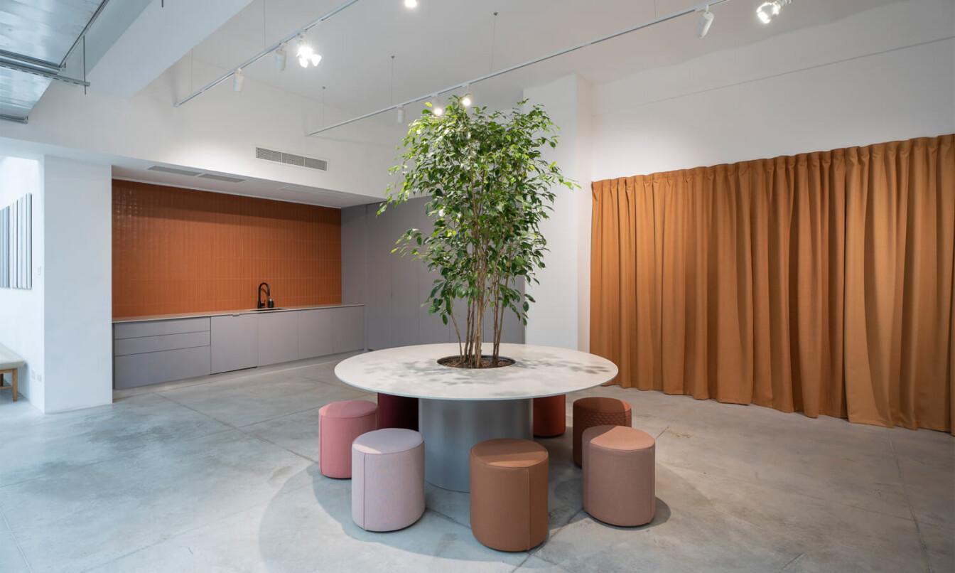 A light colored office kitchen with orange fabric details and a colorful round seating area in front.
