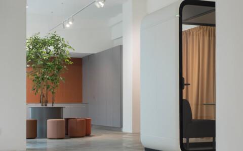 A white space with fabric chairs and a white Framery Four meeting pod peeking around the corner.