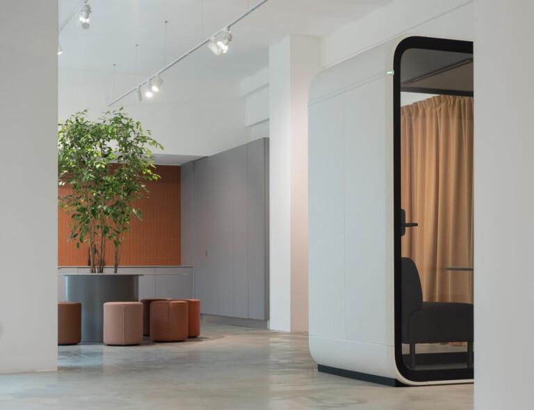 A white space with fabric chairs and a white Framery Four meeting pod peeking around the corner.