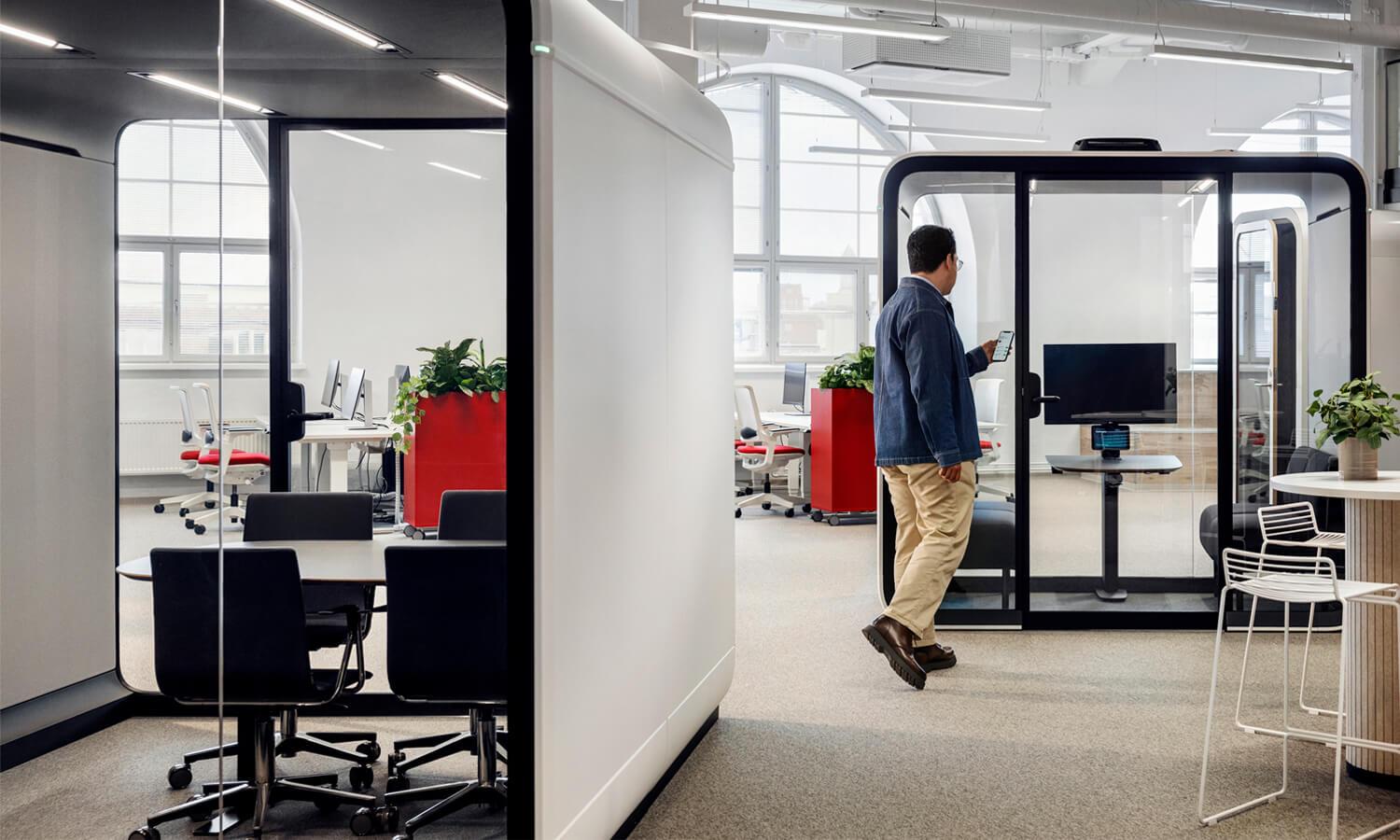 A person with phone in hand walking into a Framery Four pod.