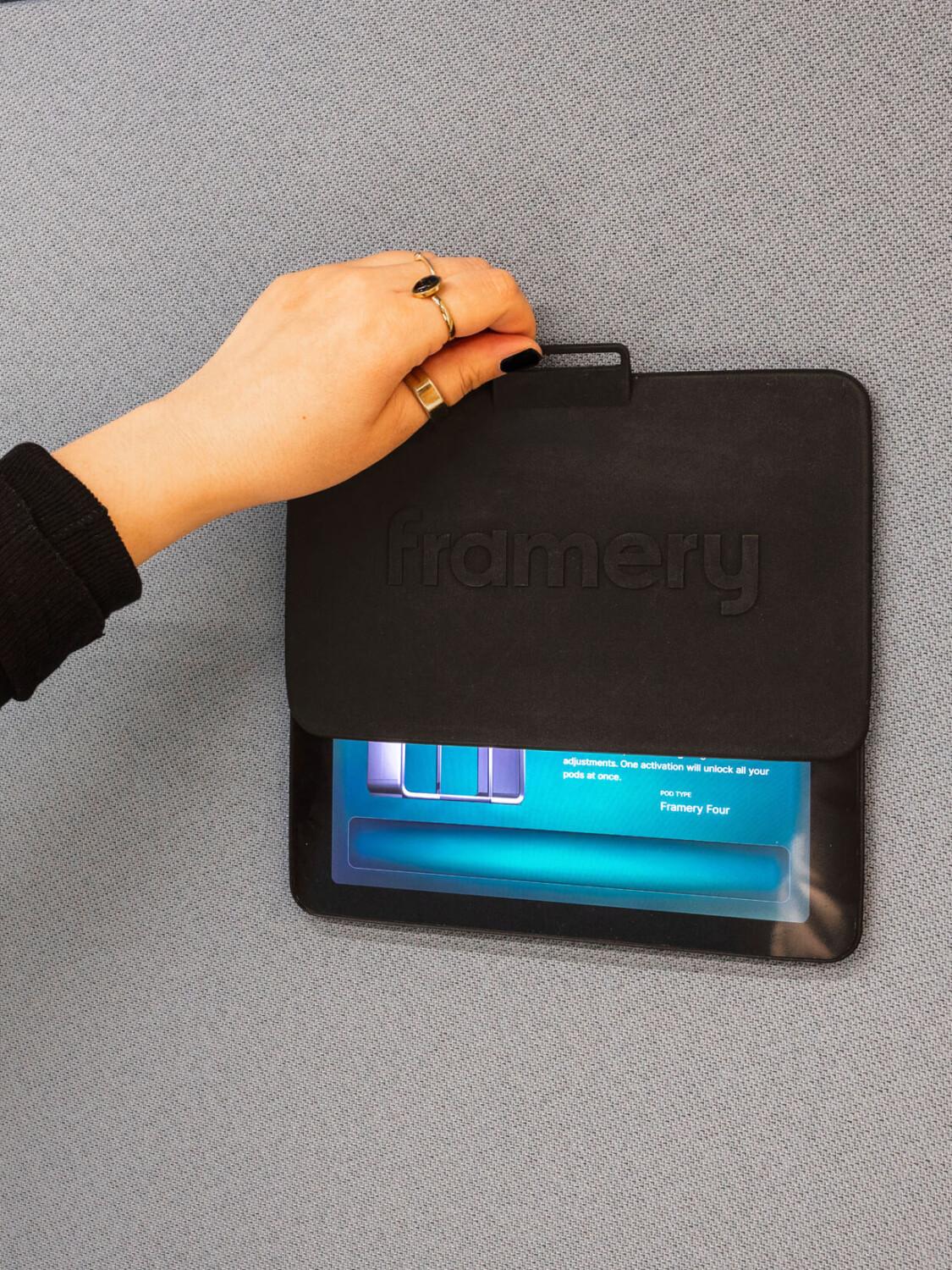 A close-up of a hand lifting a cover plate off of a Framery smart pod touch screen.