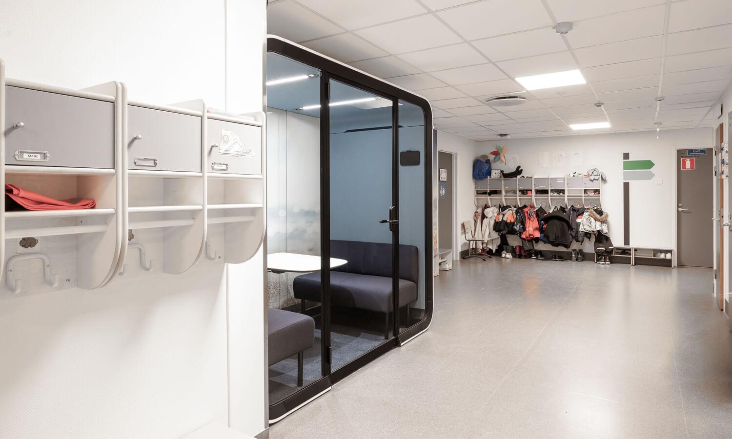 An empty school hallway with a study pod and clothes racks on walls.