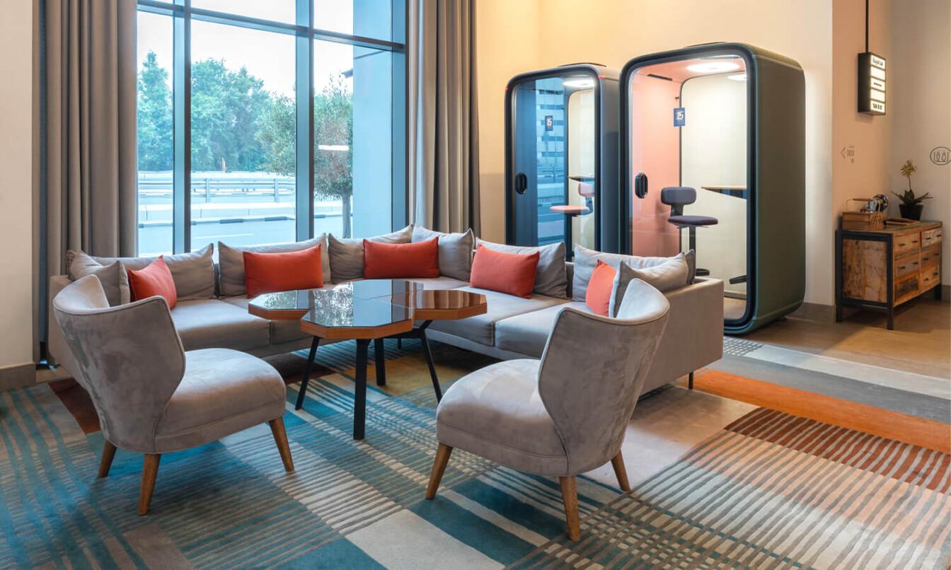 Two Framery phone booths behind a sofa group in a hotel lobby.