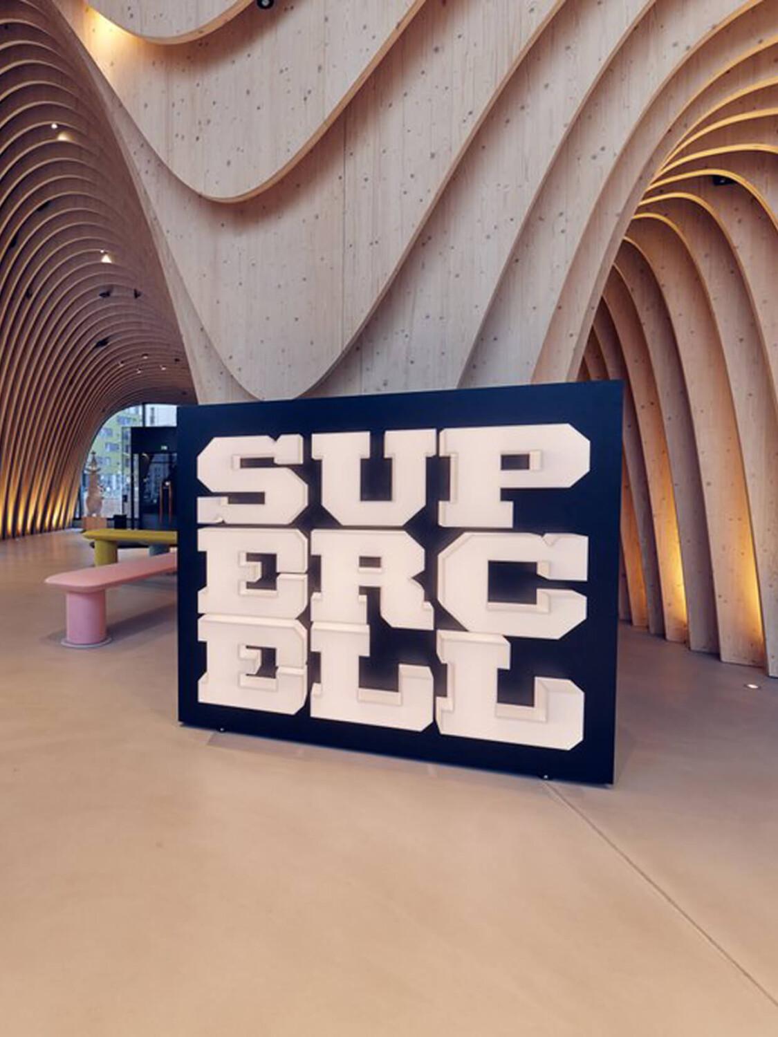 Architecture with curved wooden panels and large "SUPERCELL" sign. Modern interior featuring benches and textured walls in a spacious, open layout.