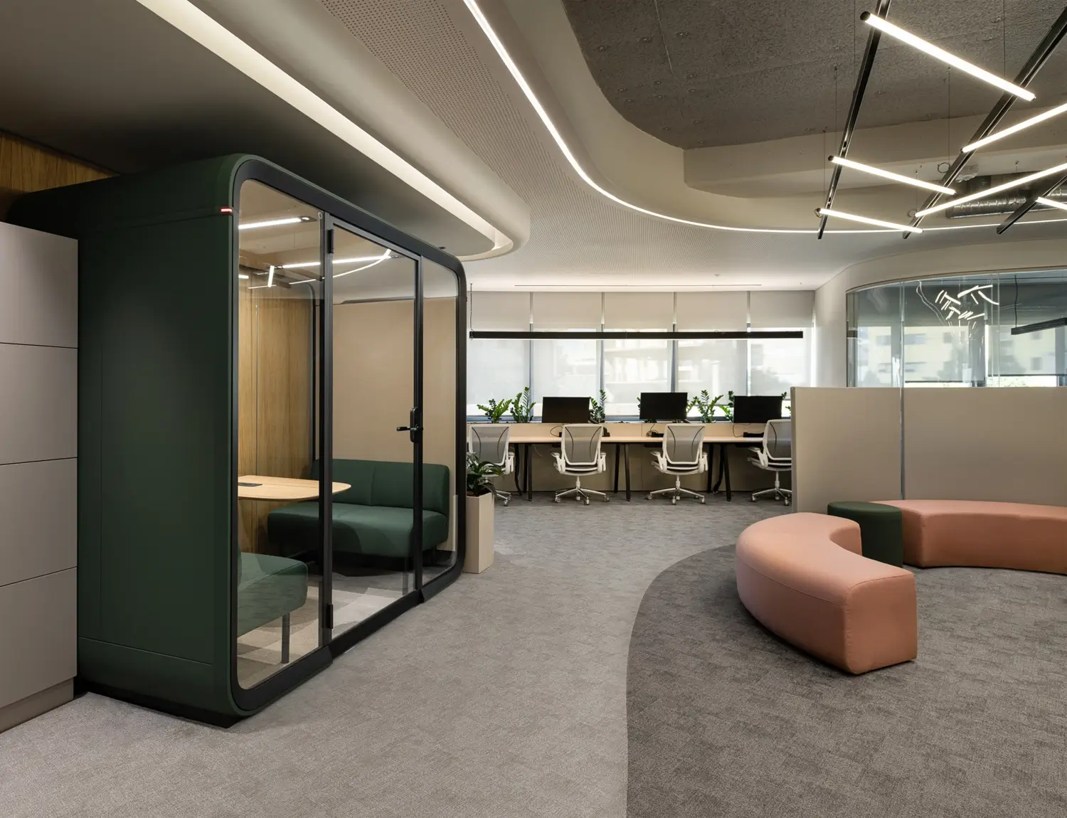 Modern and multifunctional office space with a green Framery Four meeting pod, curved seating, workstations, and sleek lighting. Bright, open layout promotes collaboration and productivity.