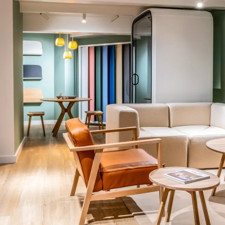 Cozy modern lounge with a beige sectional sofa, a brown leather armchair, and round coffee tables on a wooden floor, with colorful vertical panels in the background.
