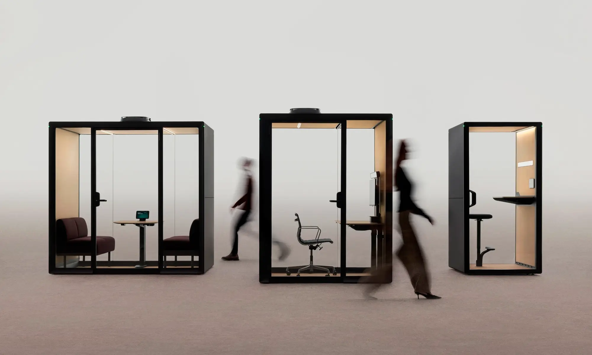 Three glass-walled Framery Gradus office pods with people walking past in a bright, minimalist space.