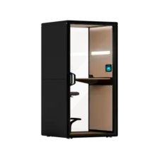 A black private office pod with a glass door and wood-paneled interior, featuring a small desk and chair.