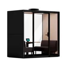 A modern black glass-walled office pod with a small desk, laptop, and seating inside.