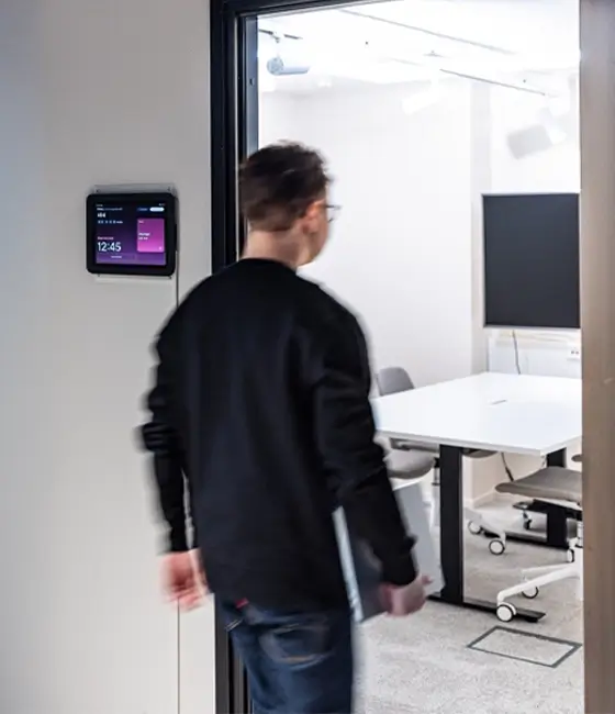 A person in a black jacket walks into a bright, modern conference room viewed from the doorway.
