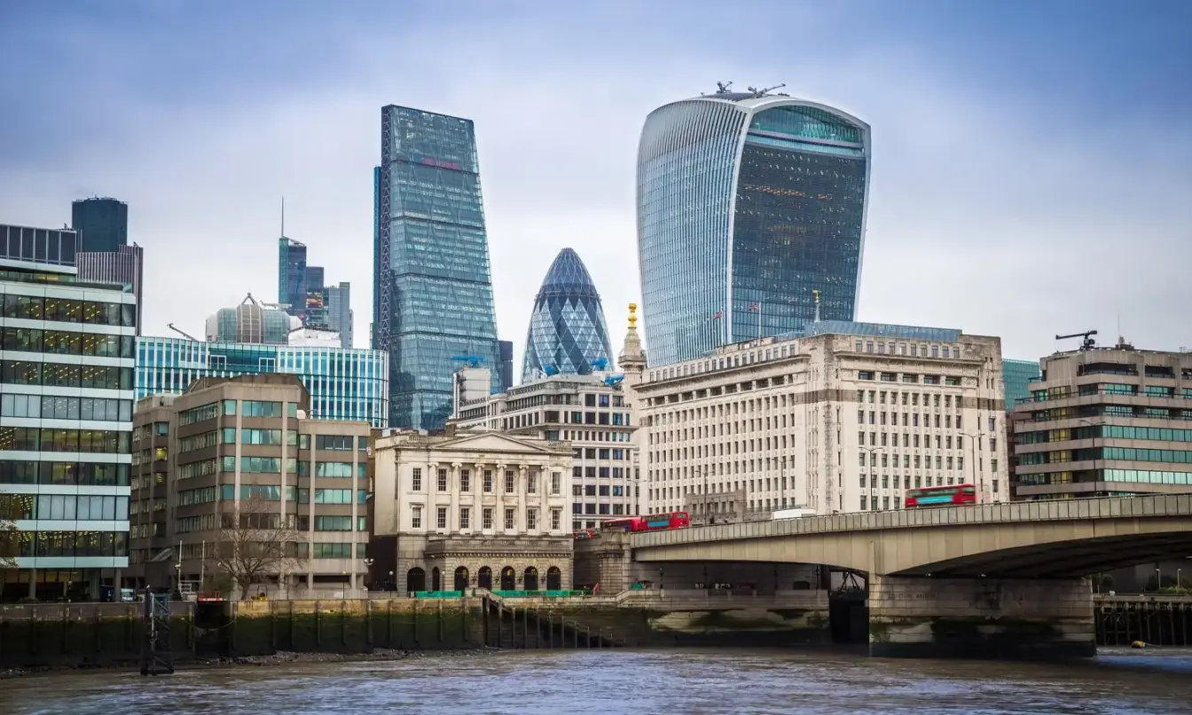 London skyline with modern glass skyscrapers along the River Thames and a bridge in the foreground.