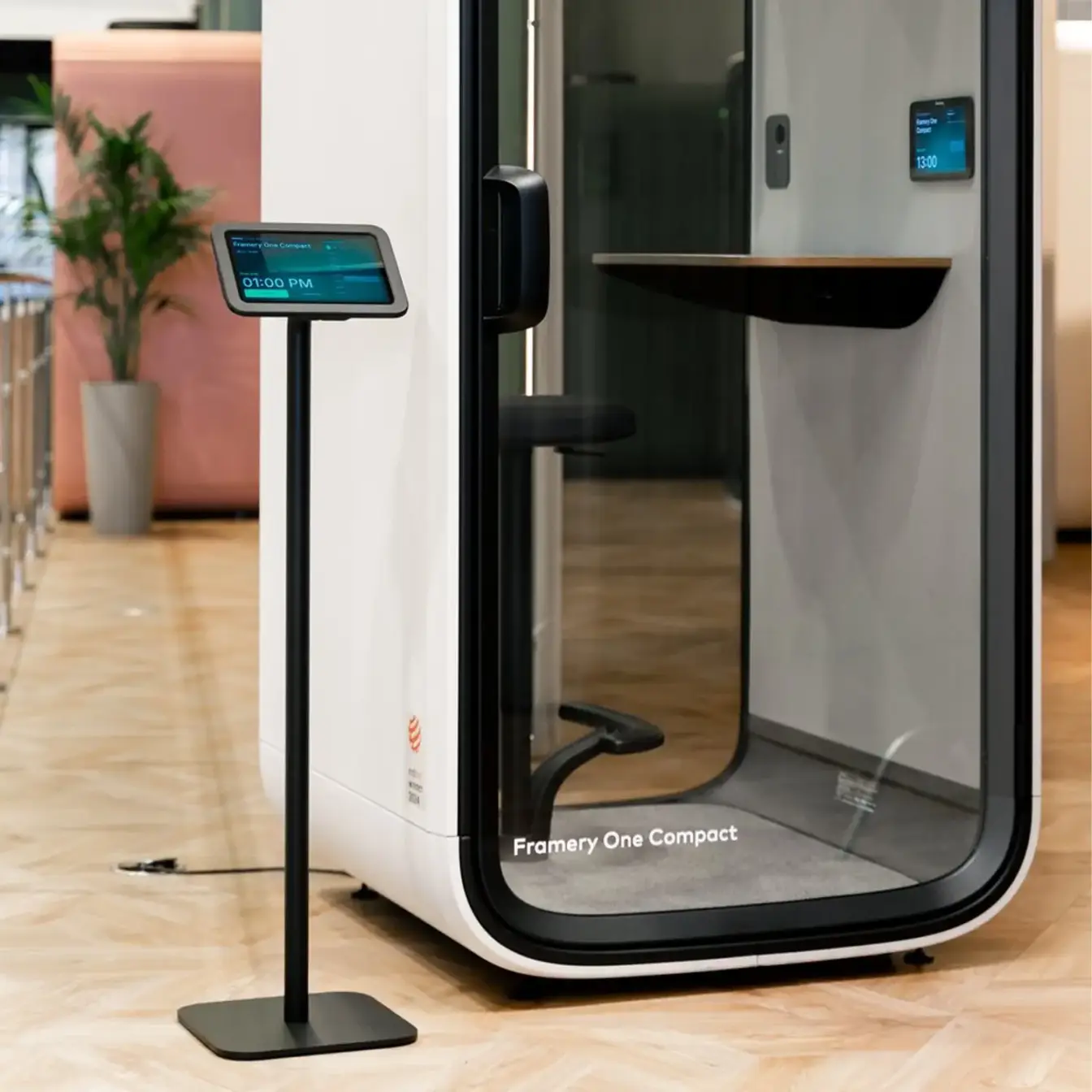 Framery One Compact smart pod in an office, with a standing touchscreen sign outside the door.